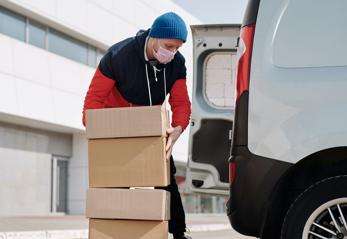 kurier dostawca wkłada paczki do samochodu jest w maseczce antywirusowej